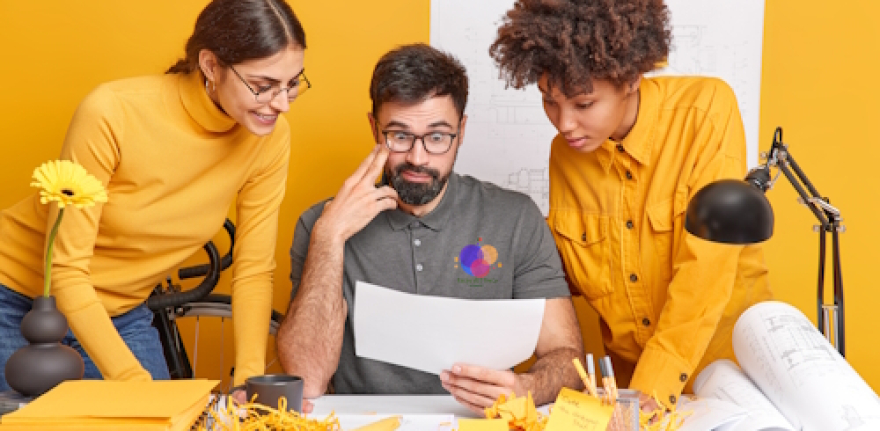 Multicultural partners cooperate on design project discuss ideas look attentively at illustration on paper brainstroming together at blueprint sketches pose in coworking space. Diverse professionals