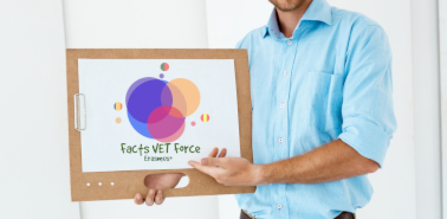 Picture of young handsome cheerful smiling businessman standing at table holding wooden clipboard with white sheet pointing on it. Light modern office interior background.